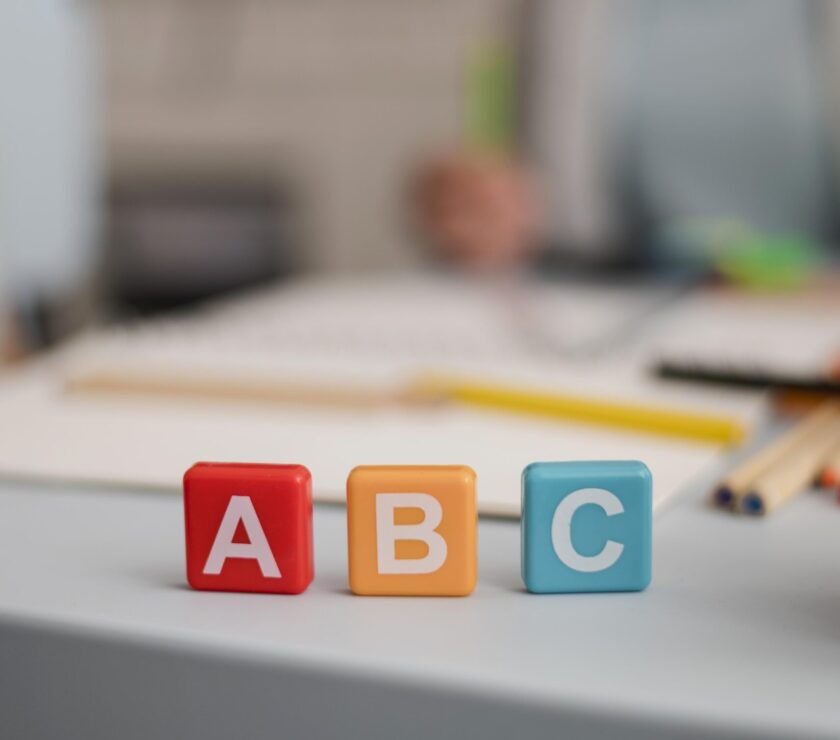 vorderansicht-von-buchstaben-auf-wurfeln-mit-defokussierter-nachhilfesitzung-im-rucken